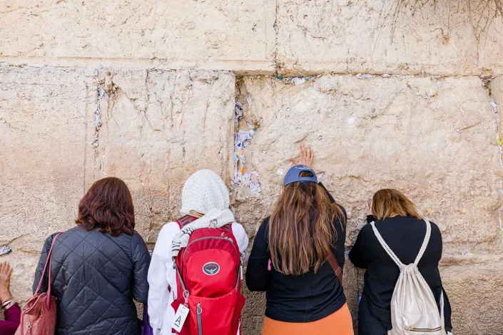 Group of women standing in prayer at the Western Wall, which is filled with prayer notes.