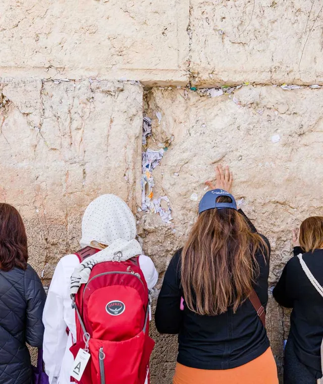 Group of women standing in prayer at the Western Wall, which is filled with prayer notes.