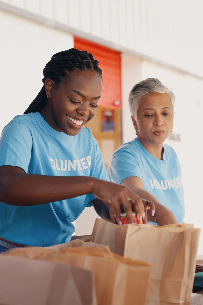 Two women putting food in brown paper bags